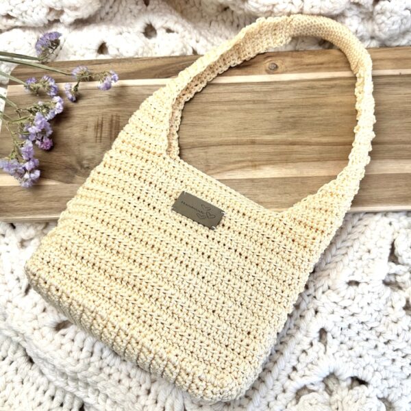 Sac crocheté en fil naturel couleur crème, modèle moderne avec anse épaisse, présenté sur une table en bois avec une décoration florale. Fait main avec une seule pelote.