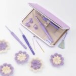 Set de crochets Tulip Etimo Purple avec étui, ciseaux, aiguilles à laine et accessoires, présenté sur fond clair avec fleurs au crochet.