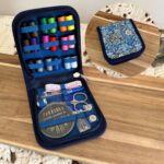 Kit de couture dans un étui rigide bleu à motif fleuri, ouvert et garni de fils, ciseaux, aiguilles et accessoires.