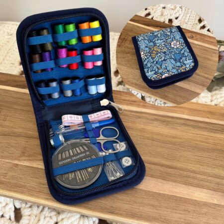 Kit de couture dans un étui rigide bleu à motif fleuri, ouvert et garni de fils, ciseaux, aiguilles et accessoires.