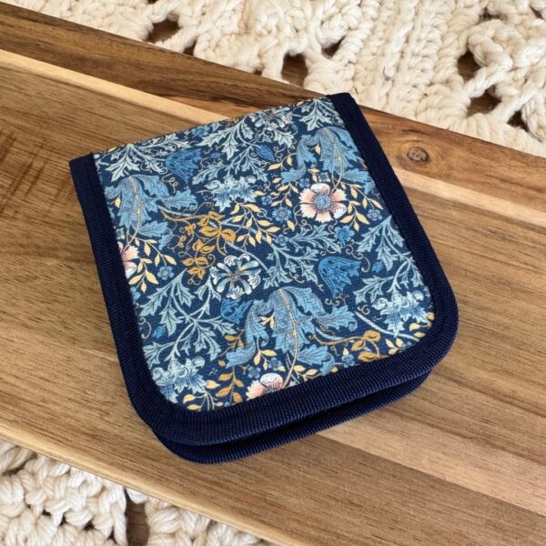 Kit de couture dans un étui rigide bleu à motif fleuri, ouvert et garni de fils, ciseaux, aiguilles et accessoires.