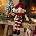 Lutin de Noël au crochet avec bonnet bordeaux, jambes rayées crème et bordeaux, chaussures noires et petites cloches dorées.