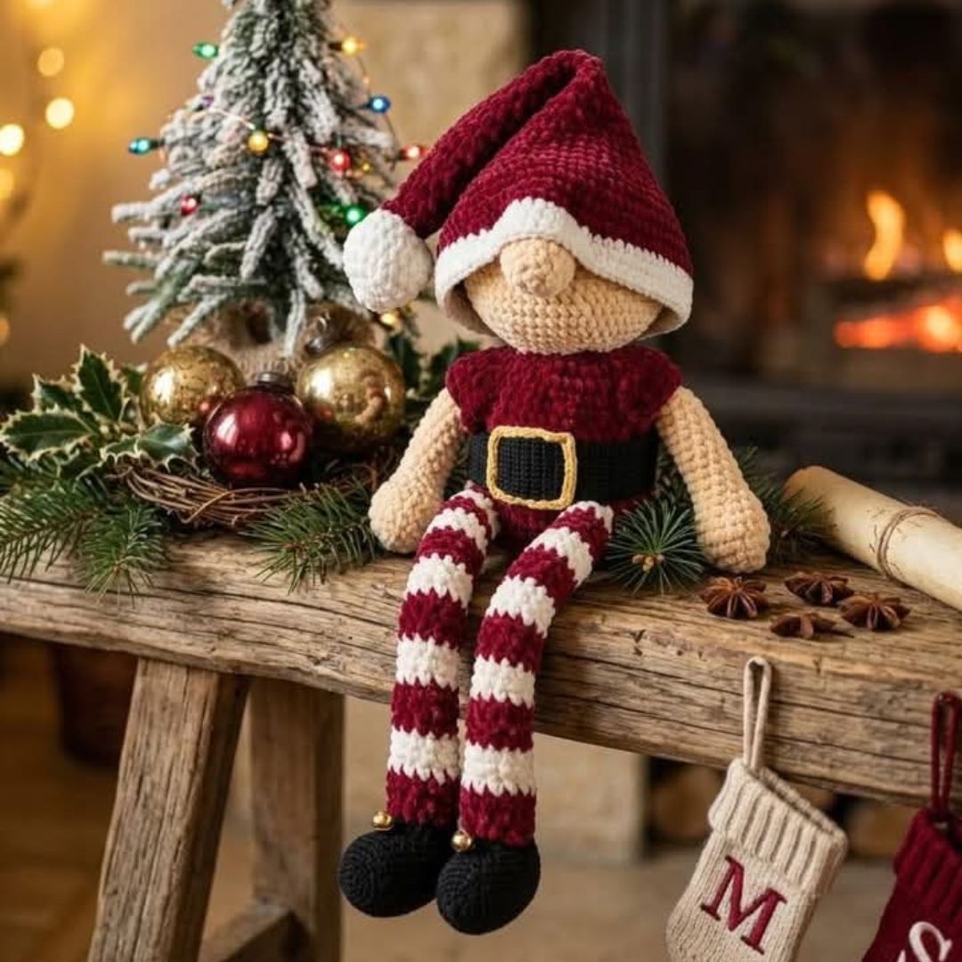 Lutin de Noël au crochet avec bonnet bordeaux, jambes rayées crème et bordeaux, chaussures noires et petites cloches dorées.